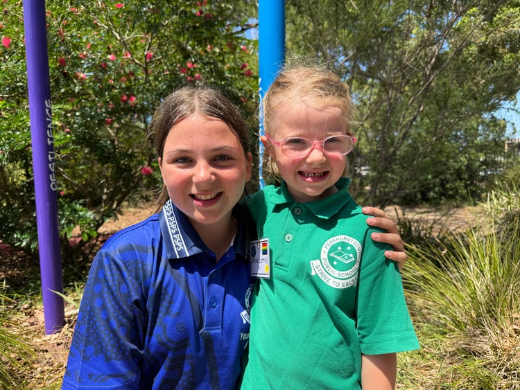 Year 6 student and Kindergarten student standing together smiling